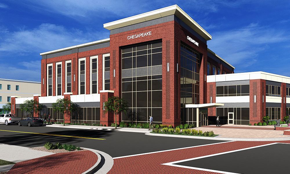 Modern red brick office building with large windows against a clear blue sky, featuring spacious parking and landscaping.