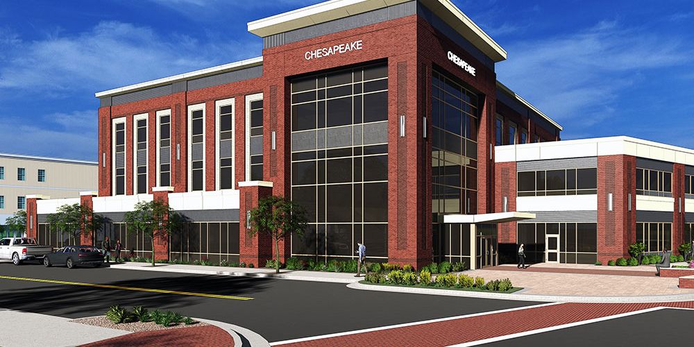 Modern office building with red brick facade, large windows, and landscaped exterior, under a clear blue sky.