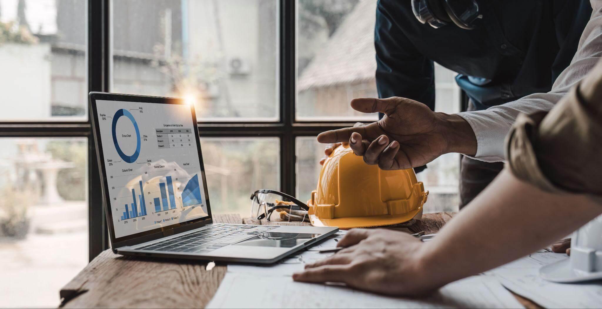 two people working on a laptop with a hard hat on top of it